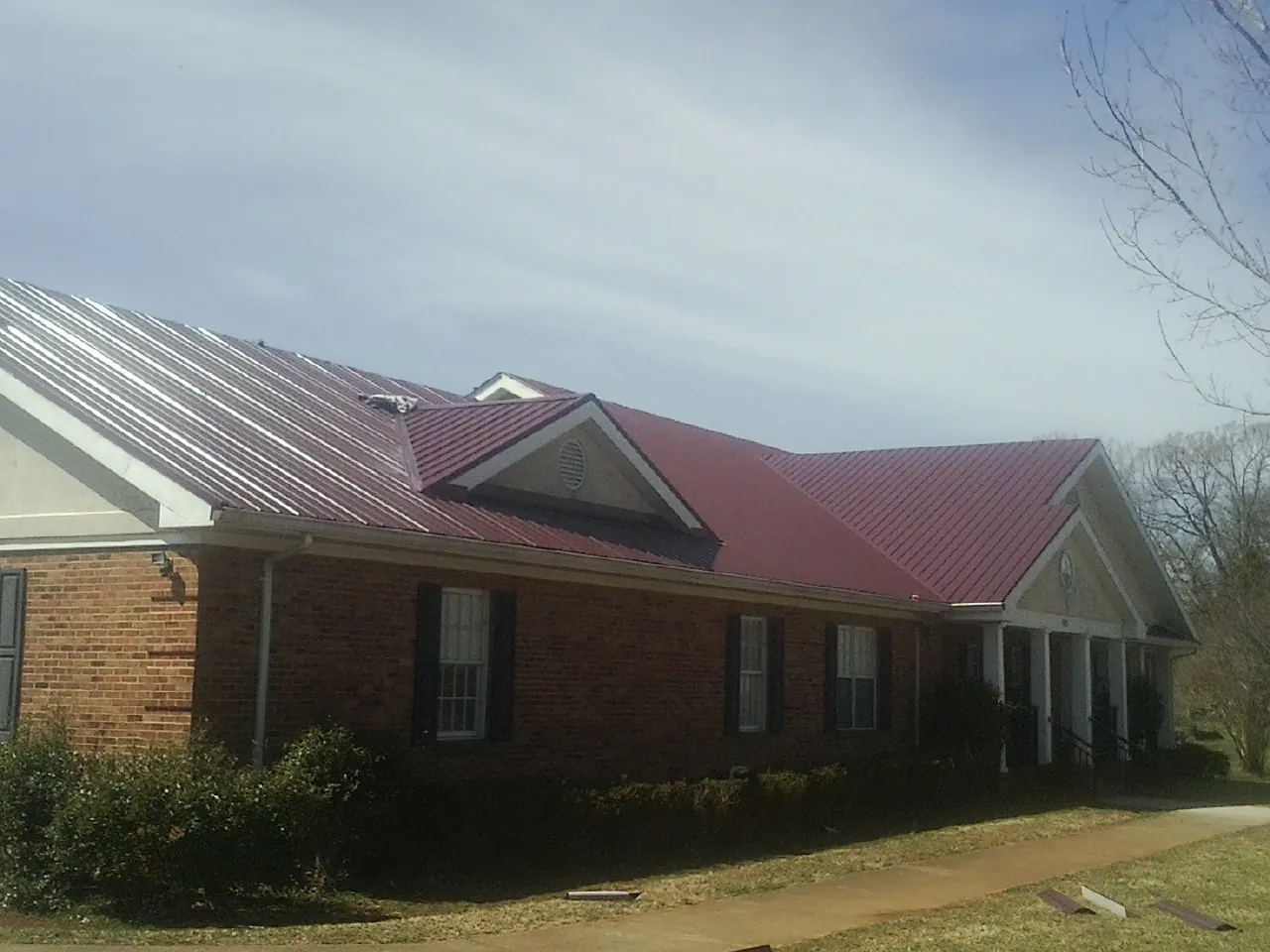 Red metal roof with gabled entries on a long brick building, from a Hail Damage Roof Repair job in Bentonia