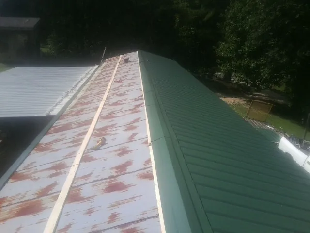 Old rusted panels beside newly installed green metal roofing — Wind Damage Roof Repair by Roofing Brothers in Bentonia