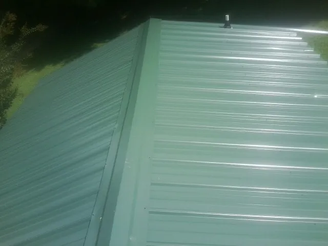 New green metal panels meeting at the ridge of a roof — Flat Roof Repair work by our crew in Bentonia