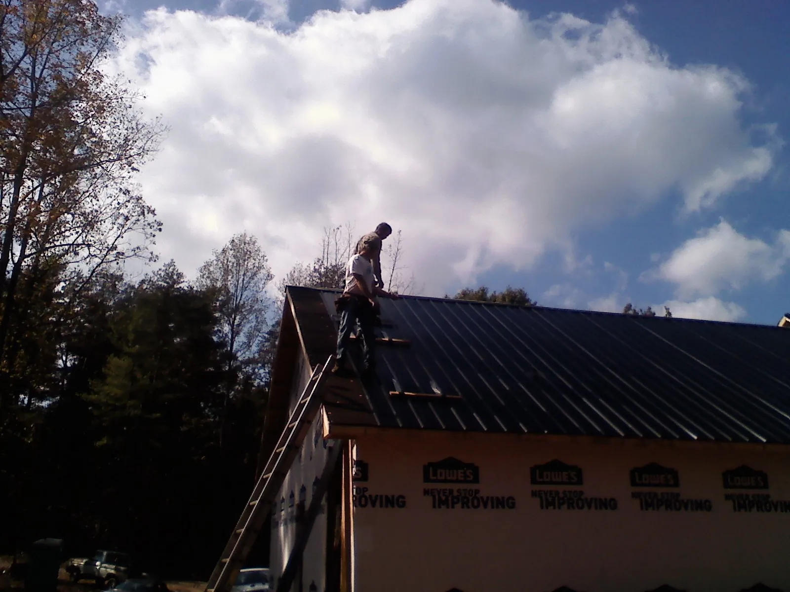 Roofer fastening dark metal panels high against a cloudy sky, from a Roof Inspection job in Bentonia